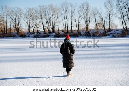 A young girl walks on a frozen lake. Panoramic view of the lake in winter. Bright cold sun. Nature walk in winter weather. High quality photo