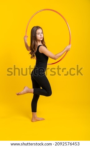 charming little girl in black sportswear performs exercises with a hoop. Good stretching and gymnastics
