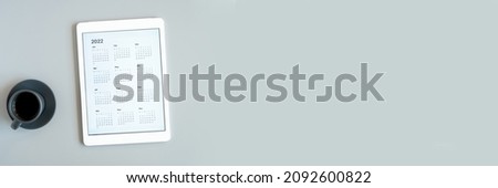 tablet computer with open app calendar for 2022 year and cup of tea or coffee on gray background. concept business or to do list goals with technology using. top view, flat lay. banner. space for text