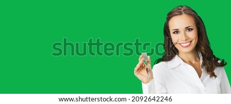 Happy smiling young businesswoman or real estate agent showing keys from new house. Portrait of brunette woman at studio, green colour background with copy space area for text. Chroma key back Royalty-Free Stock Photo #2092642246