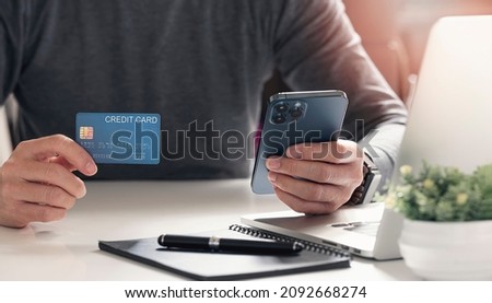 Man hand holding credit card and using smartphone at home, Businessman or entrepreneur working, Online shopping, e-commerce, internet banking, spending money. Sitting at the table.
