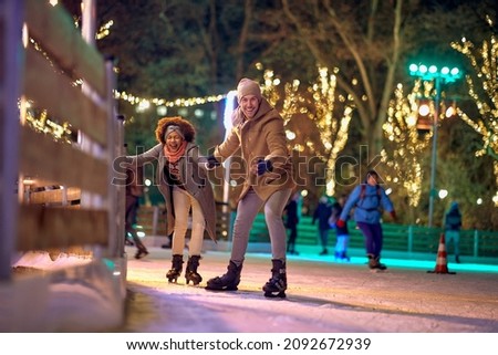 Jolly multiethnic couple enjoying night ice skating together