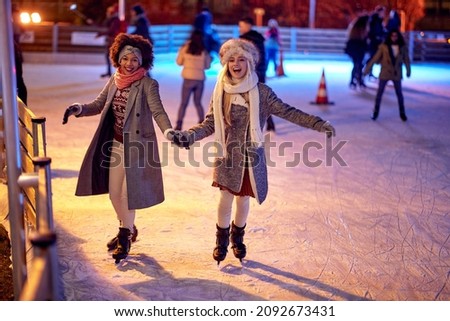 Beautiful gilfriends ice skating together at night; Winter joy concept