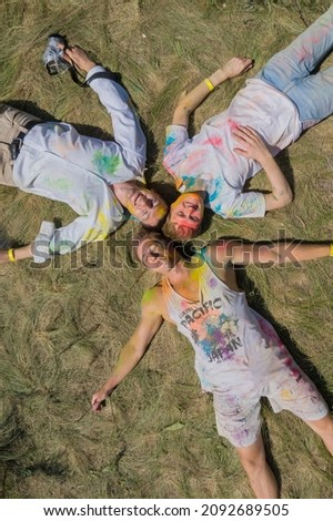 three happy men are lying on the grass close-up Holi holiday colored spots of paint on their faces sunny day smiles spots on clothes closed eyes vertical top view. High quality photo
