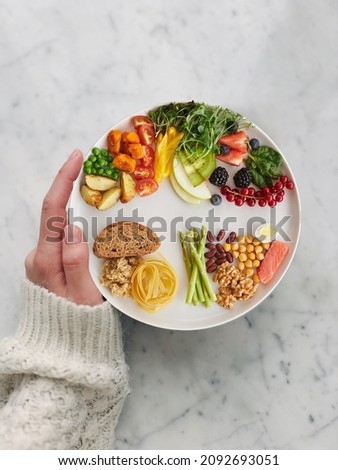 hand holding a dish of balanced colorful fruits and vegetables on granite table background top view (healthy concept)
