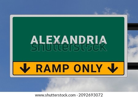 Alexandria logo. Alexandria lettering on a road sign. Signpost at entrance to Alexandria, USA. Green pointer in American style. Road sign in the United States of America. Sky in background