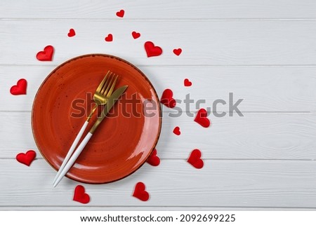  Valentines day table setting on a white wooden background top view, photo with copyspace. A red plate, golden cutlery and red hearts top view, romantic dinner concept