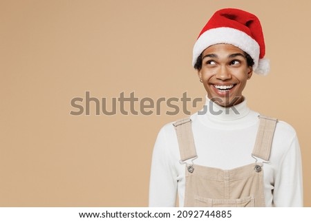 Young smiling happy african man 20s wear Santa Claus red Christmas hat look aside on copy space area isolated on plain pastel beige background studio portrait. Happy New Year 2022 celebration concept