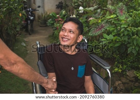 A man with a disability caused by childhood polio shakes another man's hand. Greeting a friend while outside his home.