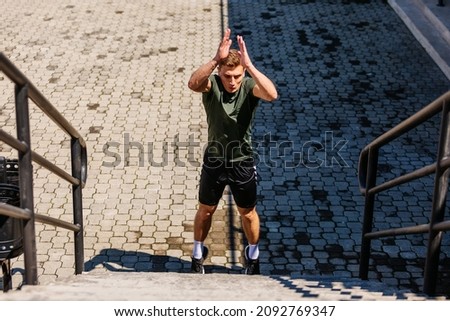Young man athlete training on a stadium. Jumping upstairs on staircase and warming up before run. Wearing casual sportswear. Central composition