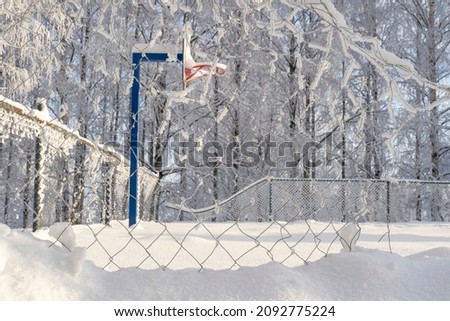 An abandoned playground with a destroyed mesh fence. A snow-covered basketball court with a ring. The concept of the winter off-season.