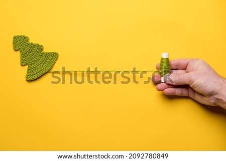 Knitted Christmas tree - a symbol of the New Year and a hand unwinding a spool of thread, on a yellow background. Copy space. 