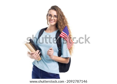 Smiling student woman in glasses with backpack holds books, notebooks and flag USA while on white studio background Royalty-Free Stock Photo #2092787146