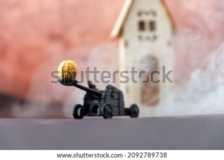 funny diorama of a catapult while pulling a peanut on a wooden house, steaming composition. High quality photo