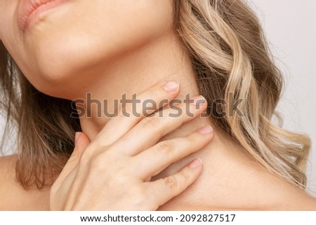 A cropped shot of a young blonde woman touching the neck with her hand hiding wrinkles, age-related changes, lines isolated on a white background. Sore throat