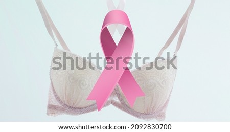 Composition of pink breast cancer ribbon on white bra against white background, copy space. breast cancer awareness campaign concept.