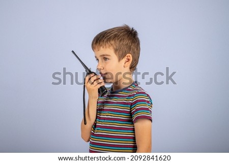 The boy is talking on the radio. A professional walkie-talkie in the child's hand. The child speaks into a walkie-talkie on a blue background. Boys' games. Royalty-Free Stock Photo #2092841620