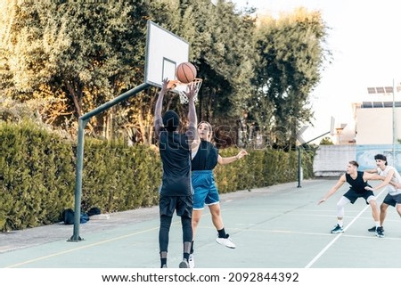 Four diverse people playing basketball in a public outdoor court