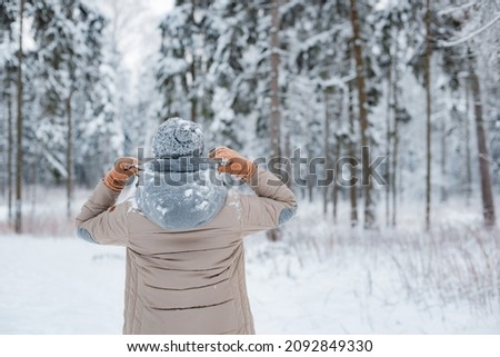 happy woman walking outside woods snowy winter day. woman mittens dressed fashionable gray stands with her back against background snowy winter forest