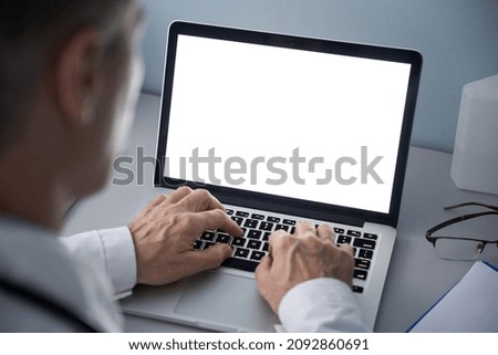Male doctor using laptop computer with blank white mockup screen technology for tele medicine medical healthcare tech website ad concept, video call e telehealth online appointment. Over shoulder view Royalty-Free Stock Photo #2092860691