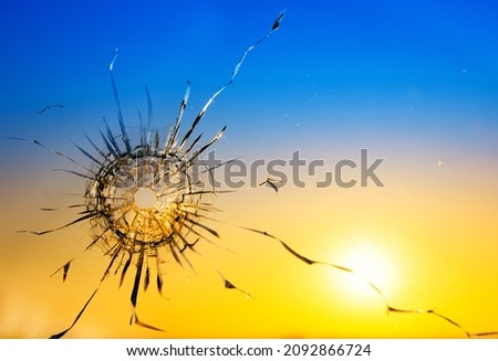 War threat concept. Hole in the glass from a bullet on the background of the flag of Ukraine Royalty-Free Stock Photo #2092866724