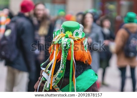 Back view of girl with red hair in hat with decorations, symbols of St. Patrick's Day, parade in city Royalty-Free Stock Photo #2092878157