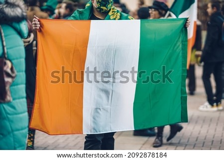 National Flag of Ireland in hands of unrecognizable man on background of people in city. Saint Patrick day holiday