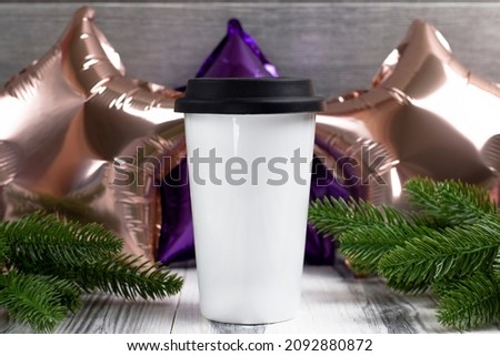White takeaway coffee cup for inscriptions or logo on a white wooden background, foil balls and a Christmas tree.