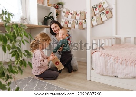 Mother with infant child having fun Christmas advent calendar tasks and gifts. Baby boy excited about festive surprise and play at home. Family celebration and preparation for New Year