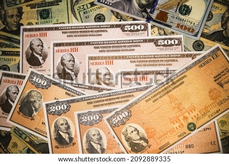 Series HH and Series EE United States Treasury Savings Bonds surrounded by US currency.  Issued by the US Government and  purchased from the U.S. Department of the Treasury. Royalty-Free Stock Photo #2092889335