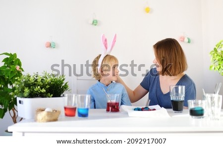 Young mother and her son are painting eggs for Easter. Child wearing funny bunny ears. Happy family preparing for Easter. Home decoration for holiday.