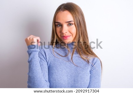Cheerful Young caucasian girl wearing blue turtleneck over white background with hand near face. Looking with glad expression at the camera after listening to good news. Confidence.
