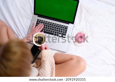 Top view woman in the morning drinks coffee works at the laptop eats donut checks mail green screen natural lighting