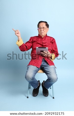 The senior Asian man wearing traditional Chinese shirt sitting on the blue background.