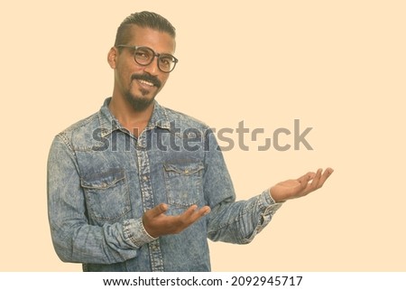 Studio shot of young bearded Indian man with denim shirt isolated against white background