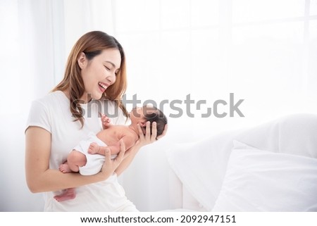 Asian loving mom carying of her newborn baby at home. Happy mum holding sleeping infant child on hands. Mother hugging her little one months old son.