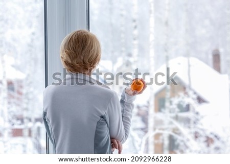 A woman standing at the window with a tangerine in her hand