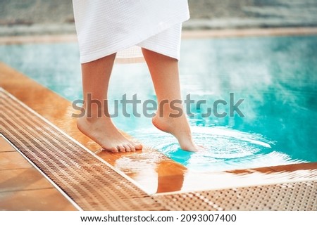 A girl puts her foot in a pool with hot thermal water, a wellness vacation at hot springs. Royalty-Free Stock Photo #2093007400