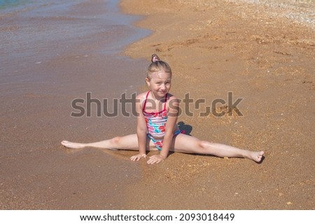 A little girl sits on a sandy seashore in a transverse twine. Summer vacation at the sea.