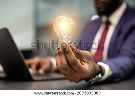 Unrecognizable african american businessman with illuminated light bulb, working on laptop at office, cropped, concept for idea, innovation and inspiration in business, business opportunities Royalty-Free Stock Photo #2093033089