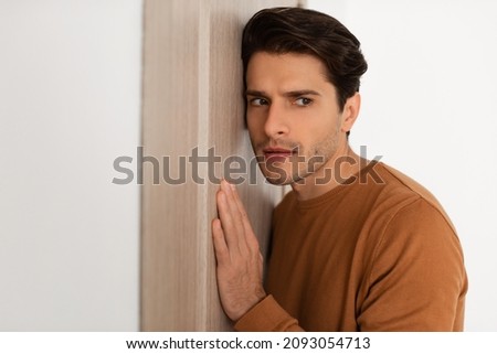 Closeup portrait of curious man eavesdropping on private conversations, spying and listening confident information through the door, handsome young guy snooping leaning on wall Royalty-Free Stock Photo #2093054713