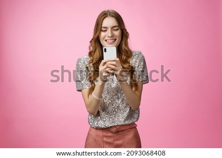 Charming glamour sociable stylish caucasian female using smartphone looking mobile phone screen look gadget display amused writing post upload photo social web page texting, pink background
