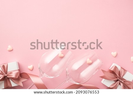 Top view photo of valentine's day decorations two wineglasses pink silk ribbon small hearts and white gift boxes with bows on isolated pastel pink background with blank space