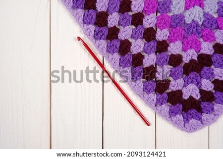 Knitted fabric,shades of purple-blue trend colors of 2022,a hook on a white wooden background.Handmade concept,pattern sample,hobby,online course on knitting fashion items,knitted interior items