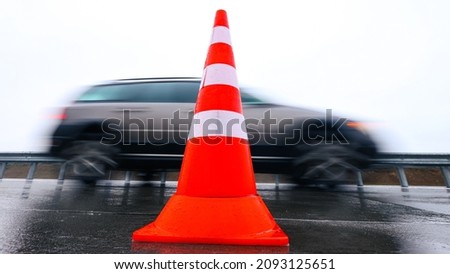 A bright traffic cone on the road against the background of a passing car