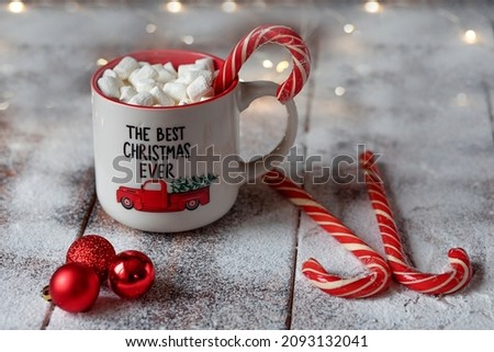 A mug of marshmallows with candy cane and christmas balls on the snow table