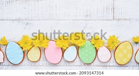 Easter greeting card with colorful rabbits, eggs, chickens and carrots gingerbread cookies on white wooden old background with copy space. Mock up. Banner. Top view.