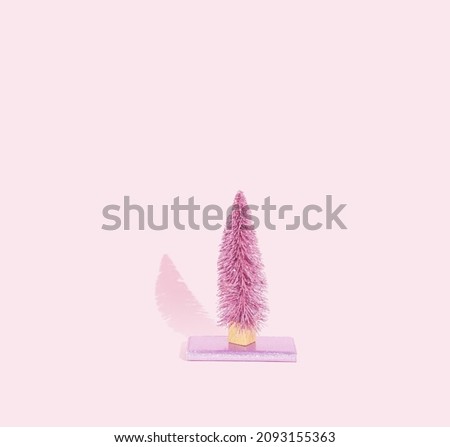 Trendy pink background, pink Christmas tree on a shiny pink cell phone case. Minimal New Year and Christmas concept.