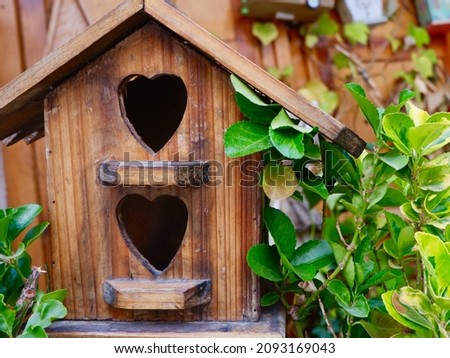 Birdhouse with heart shaped opening outside surrounded by greenery at summertime. Conceptual for family home and romantic love.