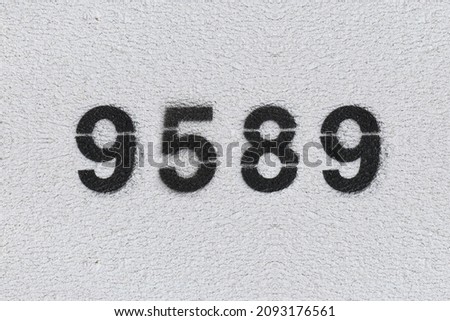 Black Number 9589 on the white wall. Spray paint. Number nine thousand five hundred and eighty nine.